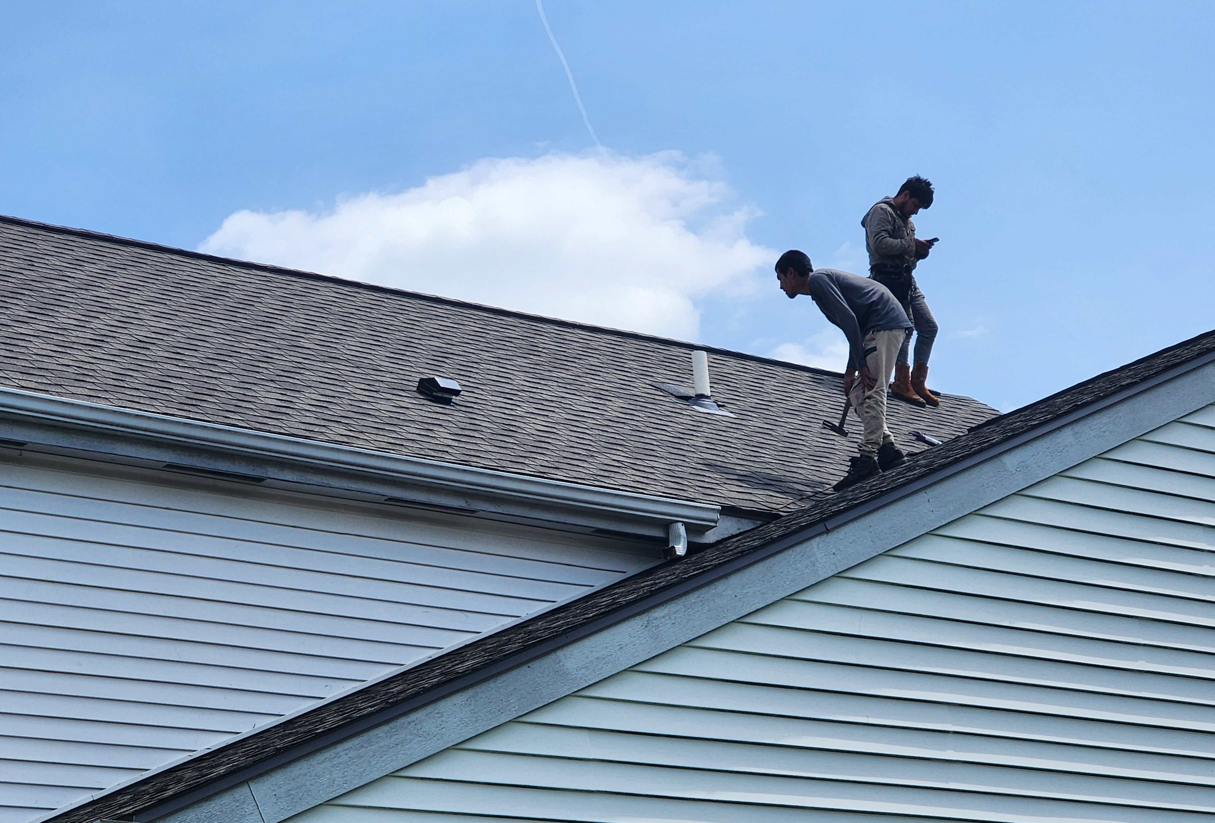 Two roofers working on a shingle roof